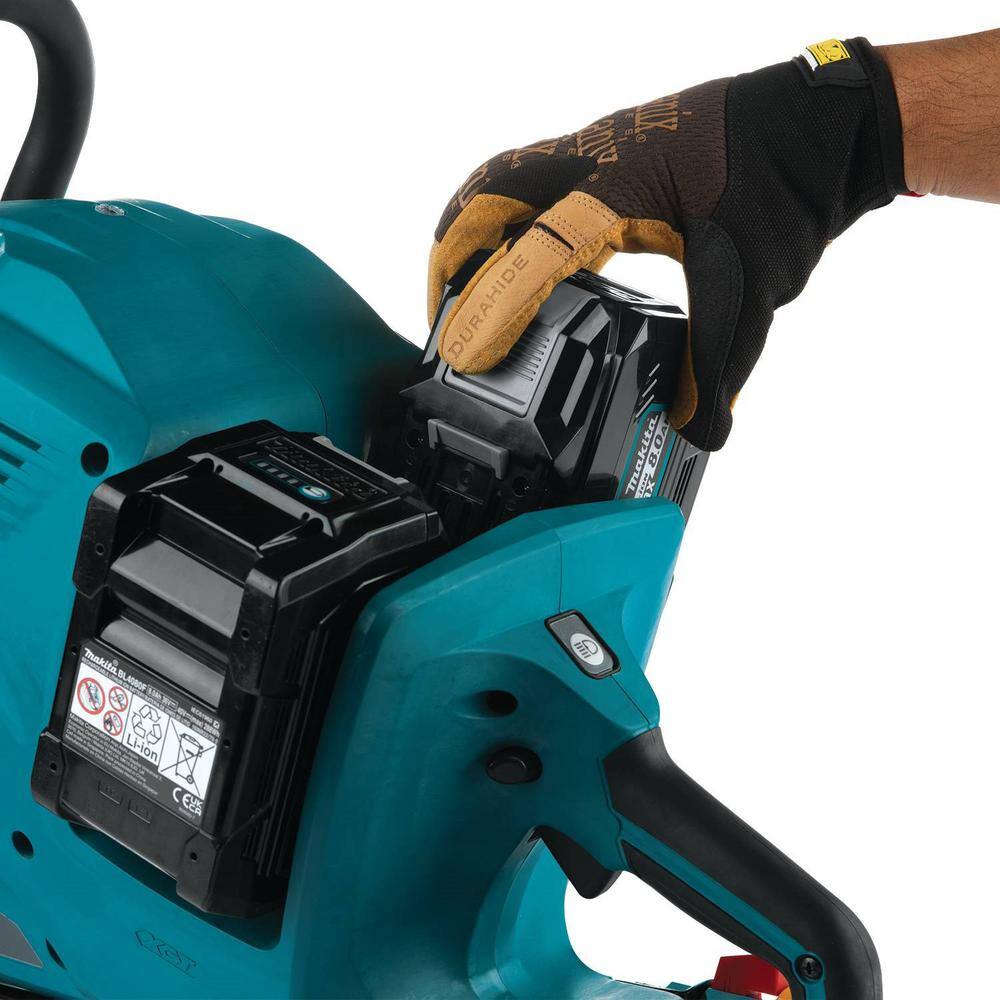 Close-up view of a hand wearing a brown and black leather utility glove loading a black Makita 40V Max XGT 8.0Ah battery pack into the rear dual-battery dock of the teal cordless 14 inch power cutter.