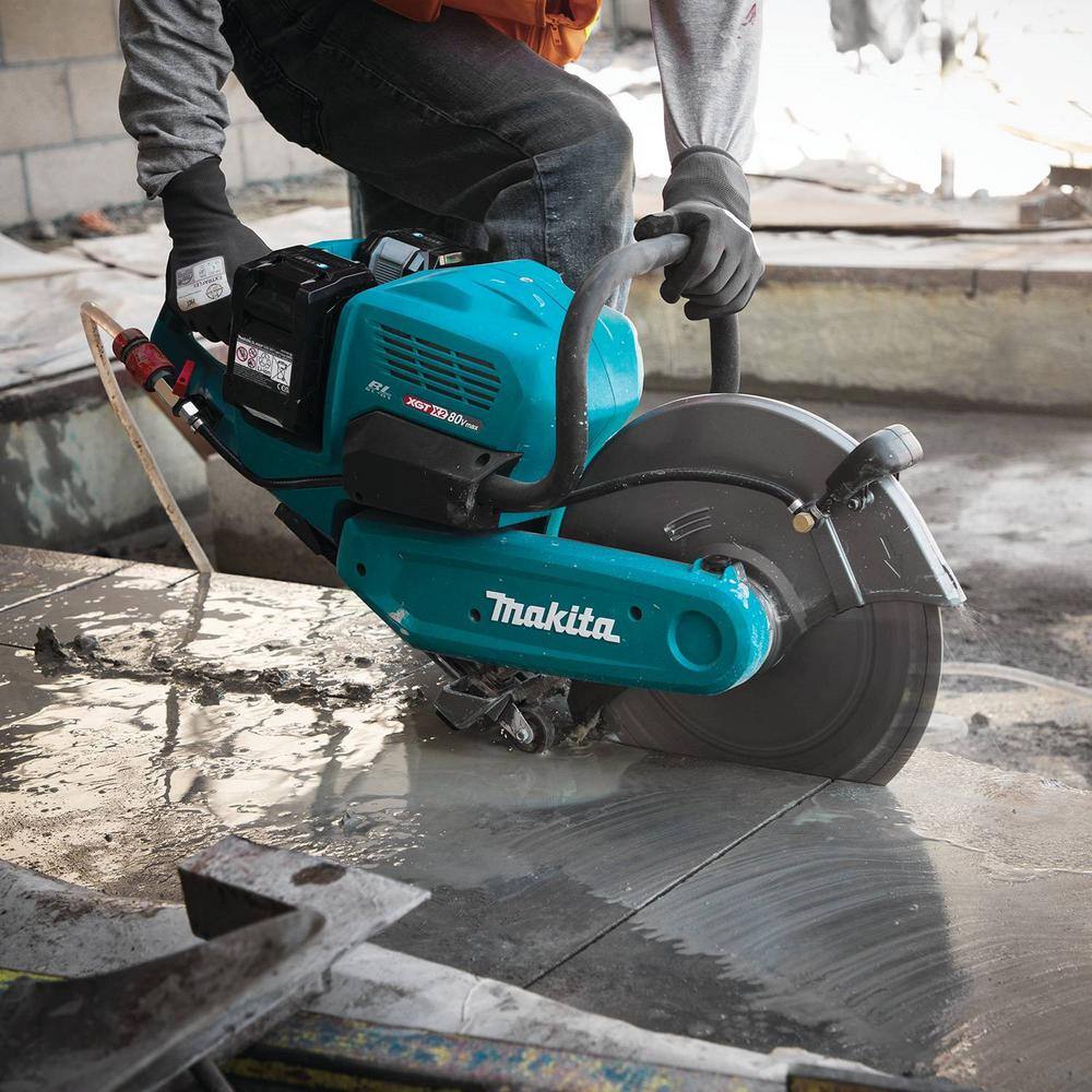 An operator using the Makita 80V Max XGT cordless power cutter to make a wet single-pass floor cut on a concrete slab, with water running over the blade path to manage silica dust on a construction jobsite.