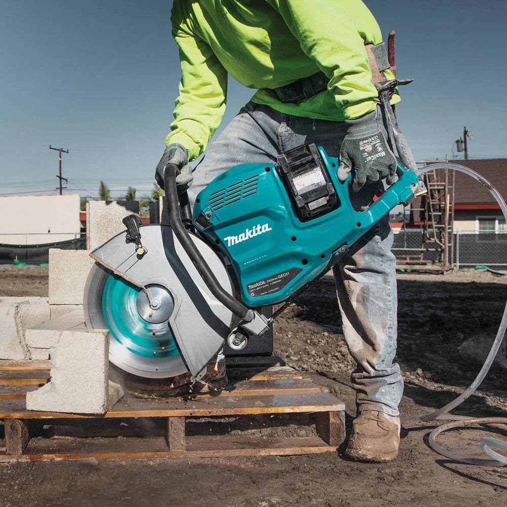 Side profile view of a construction worker using the Makita cordless power cutter to slice down through a gray structural concrete hollow block resting on a wooden pallet outdoors.