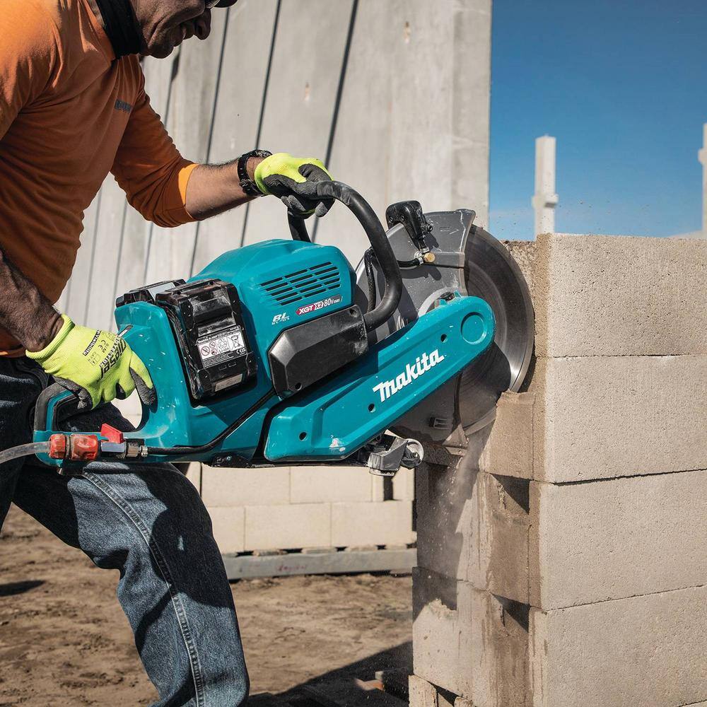 A worker using the Makita 14 inch masonry saw to perform a vertical plunge wall cut on a concrete block wall building structure, showcasing the adjustable blade guard orientation and multi-position handle usage.