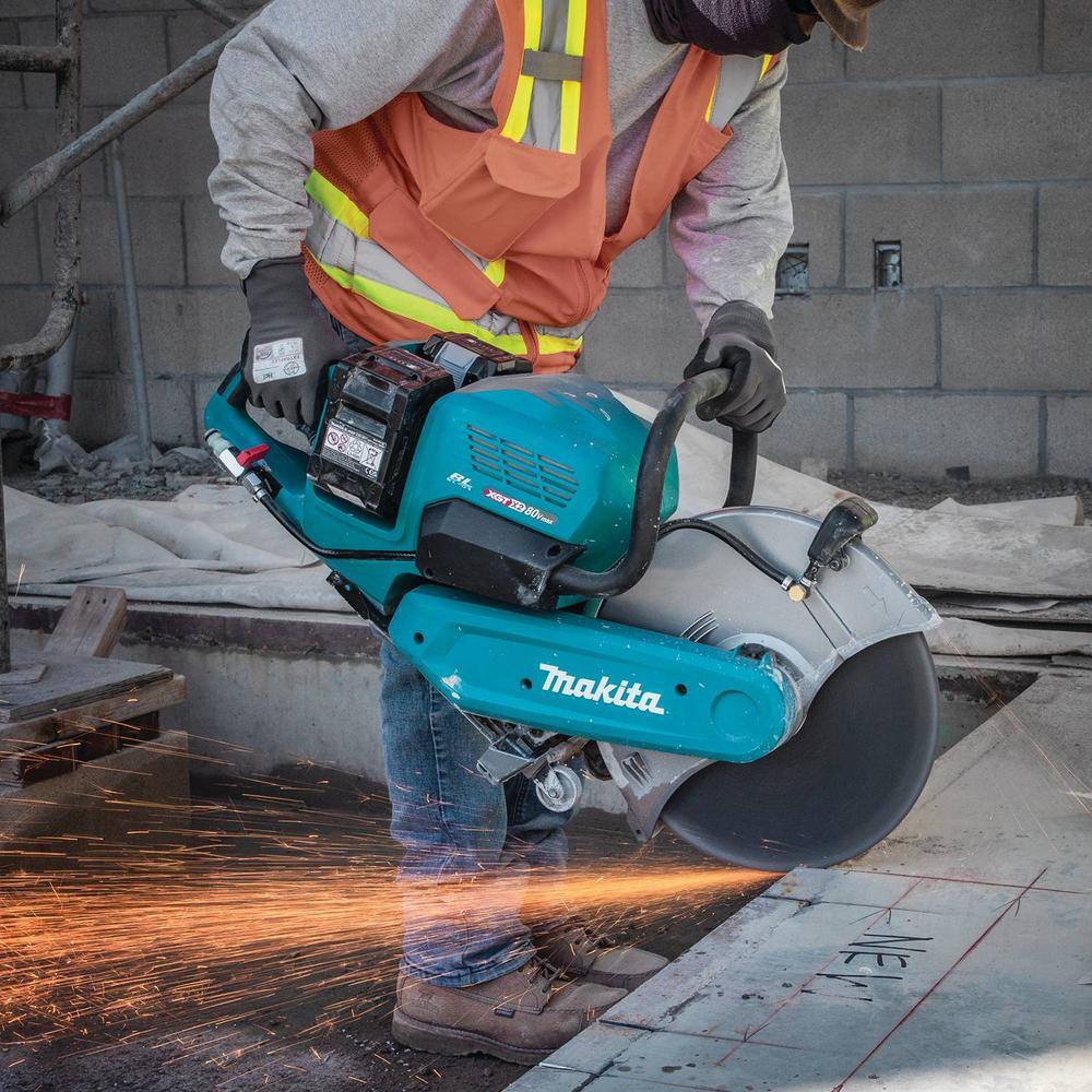 Action shot of a concrete contractor guiding the Makita cordless demolition saw along a marked layout line on a flat floor surface, sending bright sparks across the ground during structural slab modifications.