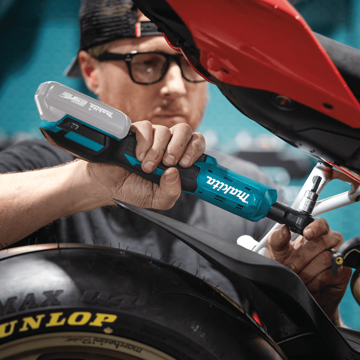 Mechanic operating the Makita XRW01Z 18V ratchet to run bolts into a motorcycle subframe beneath tight rear fender bodywork.