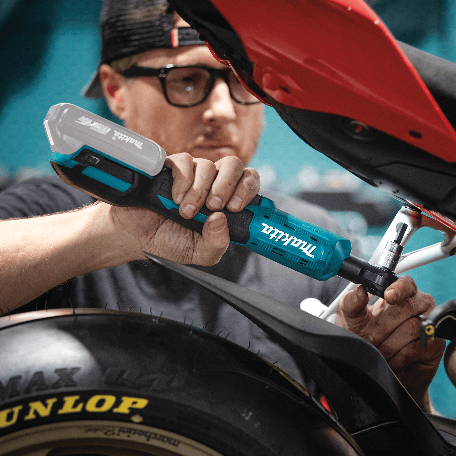 Mechanic operating the Makita XRW01Z 18V ratchet to run bolts into a motorcycle subframe beneath tight rear fender bodywork.