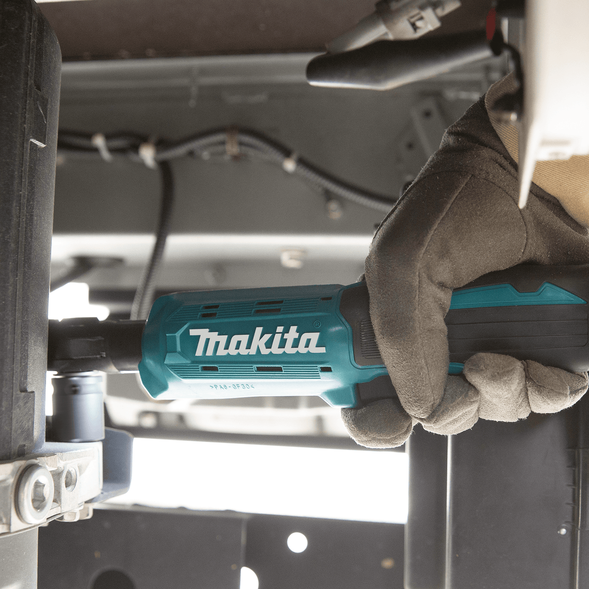 Mechanic using the low-profile Makita XRW01Z cordless ratchet to drive fasteners in a confined under-chassis vehicle compartment.