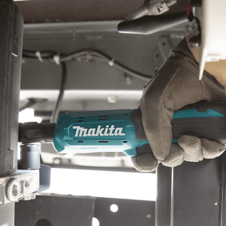 Mechanic using the low-profile Makita XRW01Z cordless ratchet to drive fasteners in a confined under-chassis vehicle compartment.