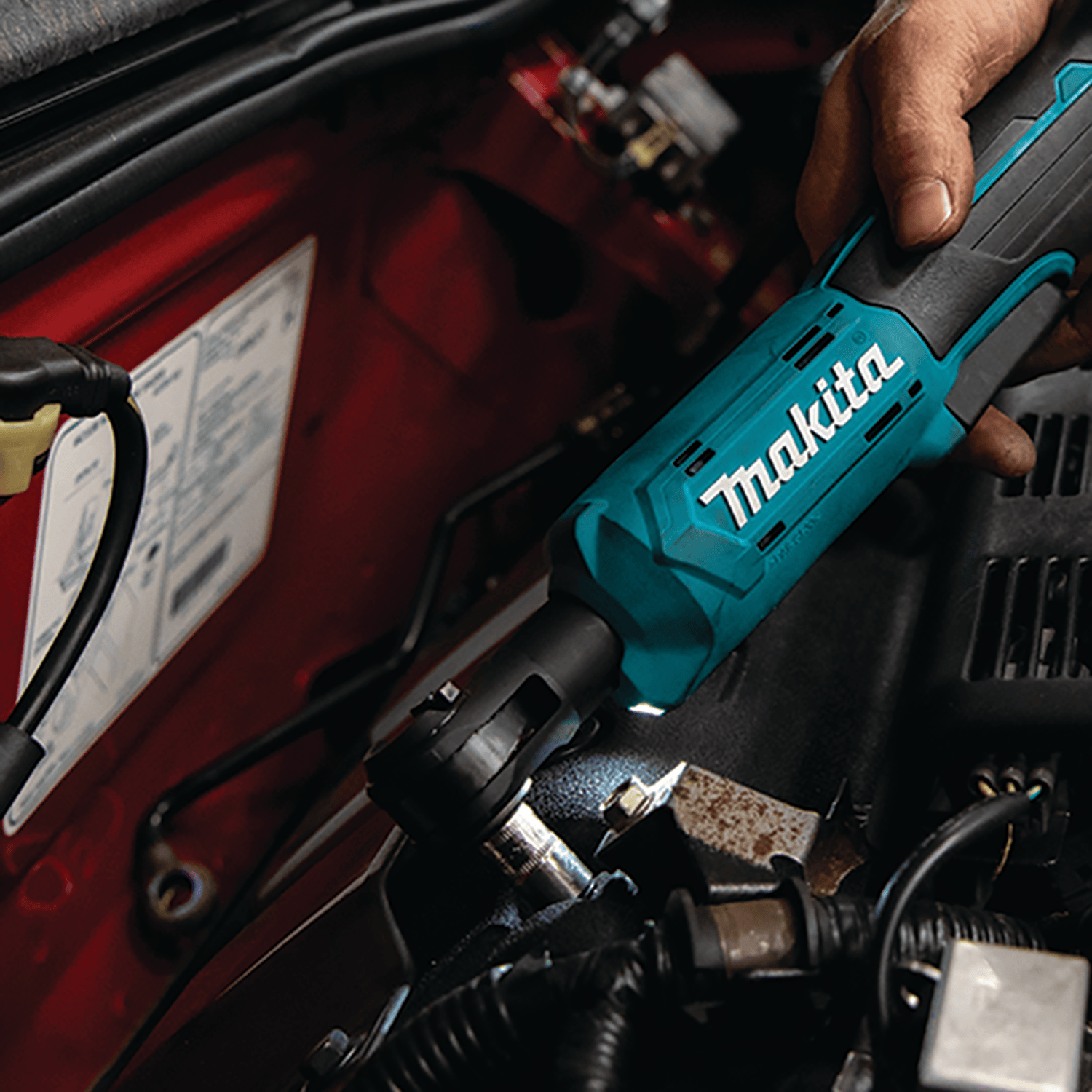 Automotive technician using the Makita XRW01Z 18V ratchet with LED illumination to loosen bolts inside a tight engine bay.
