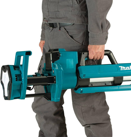A worker carrying the Makita DML813 tower light in its folded position using the integrated heavy-duty handle to demonstrate its portable 15.8-pound design.