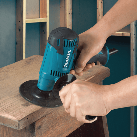 Operator using the Makita 5-inch disc sander to smooth and strip a wooden furniture surface in a workshop.