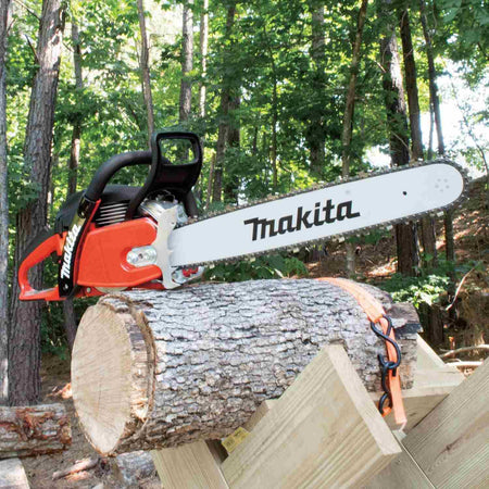 The Makita professional chainsaw resting securely on a log that is strapped to a wooden sawbuck in a forest setting.