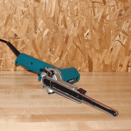 Makita 9032 3/8-inch x 21-inch detail belt sander resting on a wooden shop bench, fully assembled with an 80-grit belt.