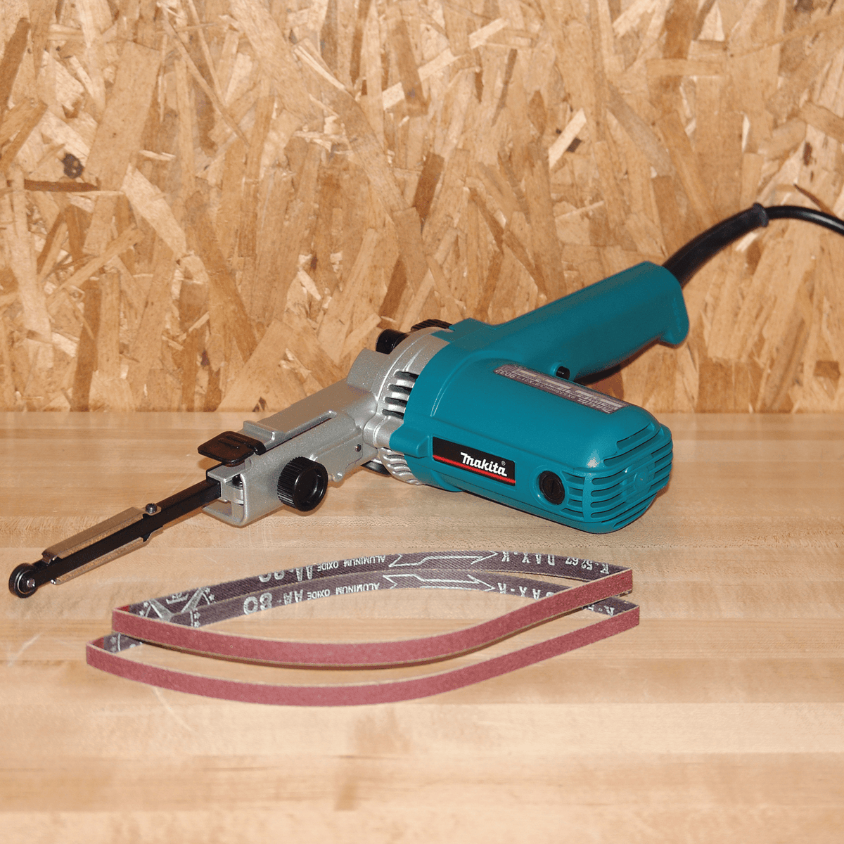 Makita 9032 3/8-inch x 21-inch detail belt sander displayed with 80-grit aluminum oxide replacement belts for woodworking and metal filing.
