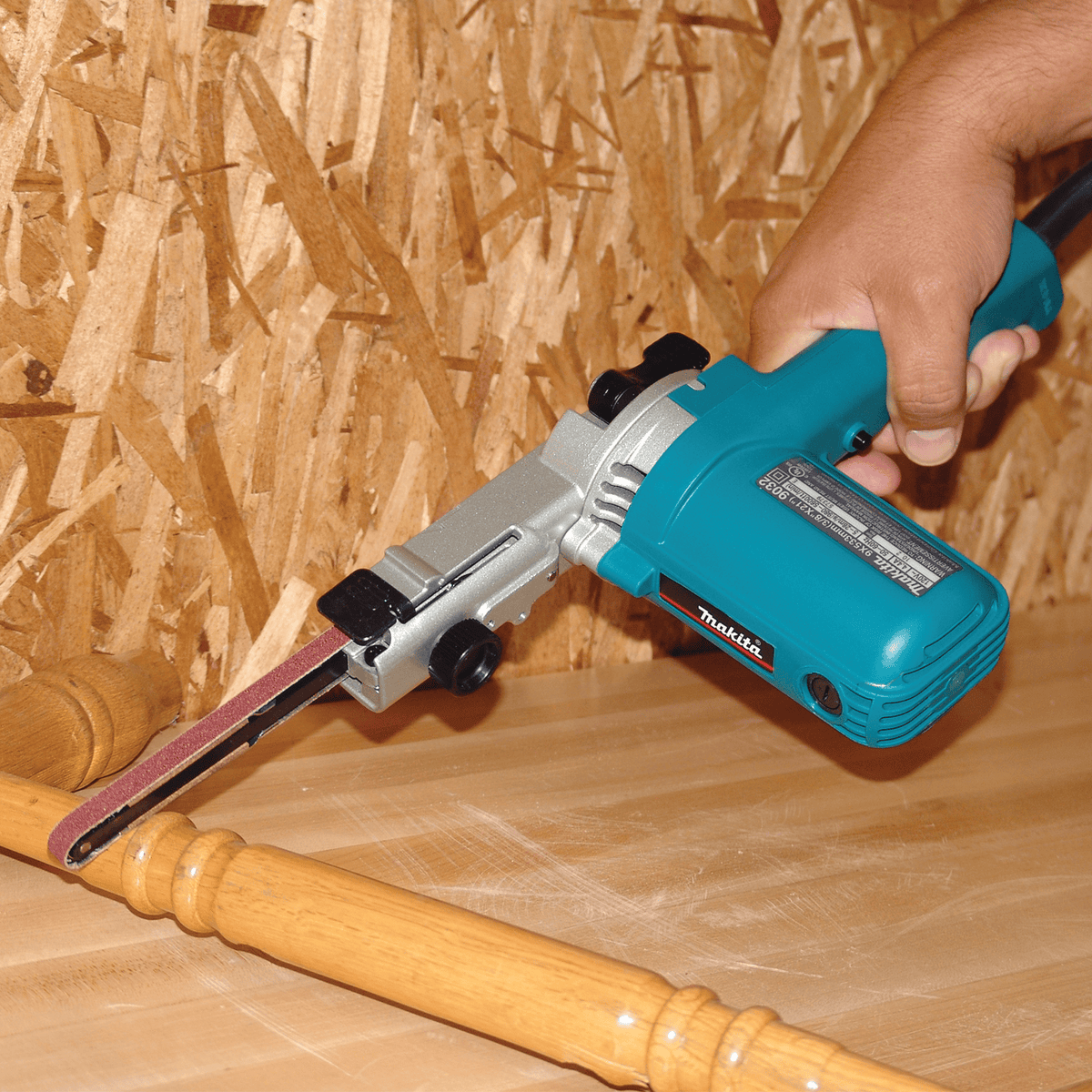 Woodworker using the Makita 9032 detail sander to shape and smooth curved wooden spindle turnings on a workbench.