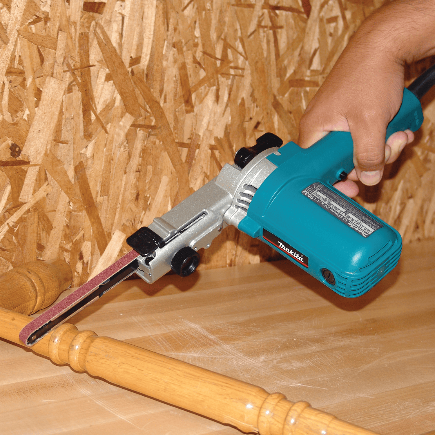 Woodworker using the Makita 9032 detail sander to shape and smooth curved wooden spindle turnings on a workbench.