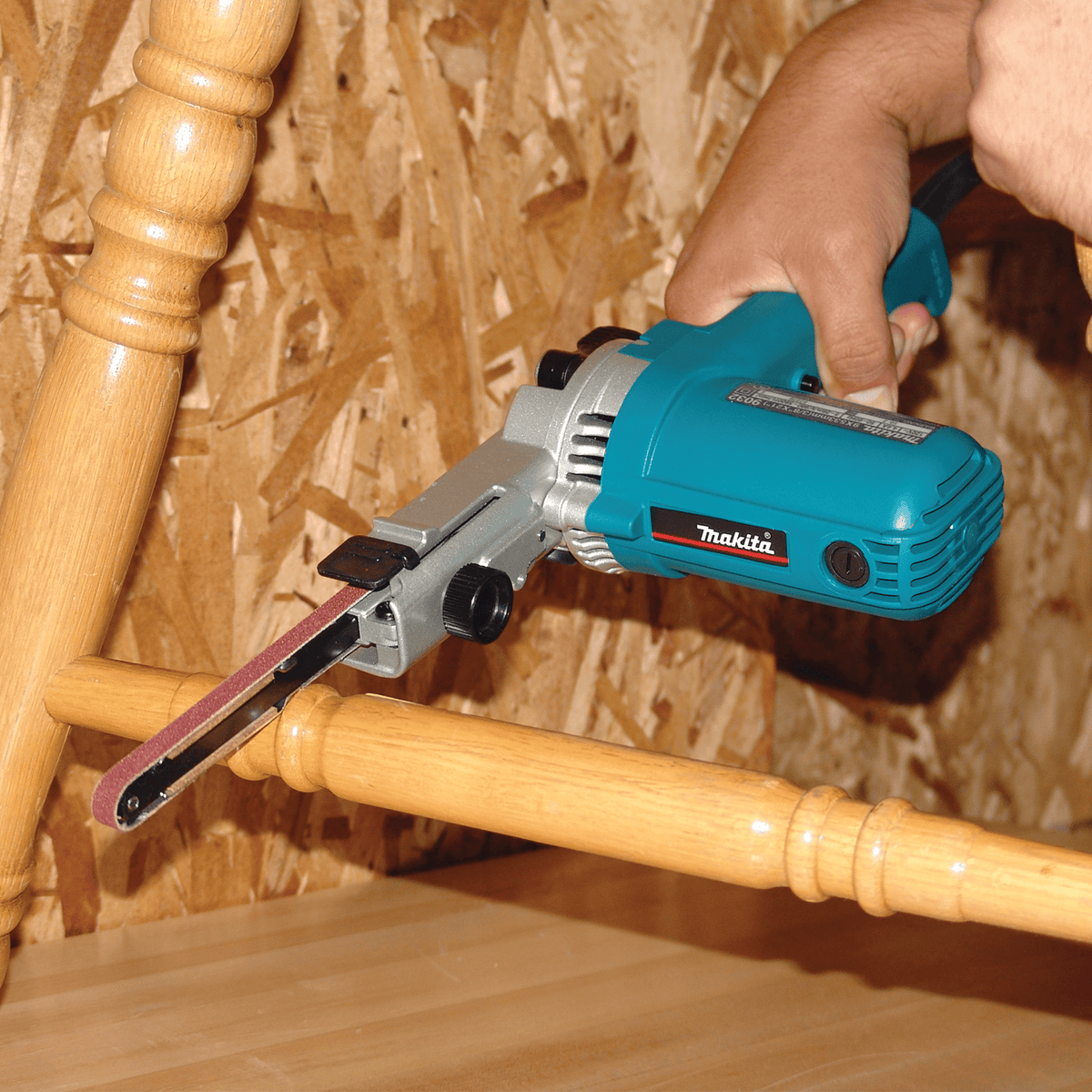 Tradesman operating the Makita 9032 belt sander to sand tight clearance gaps between wooden chair legs and rungs.