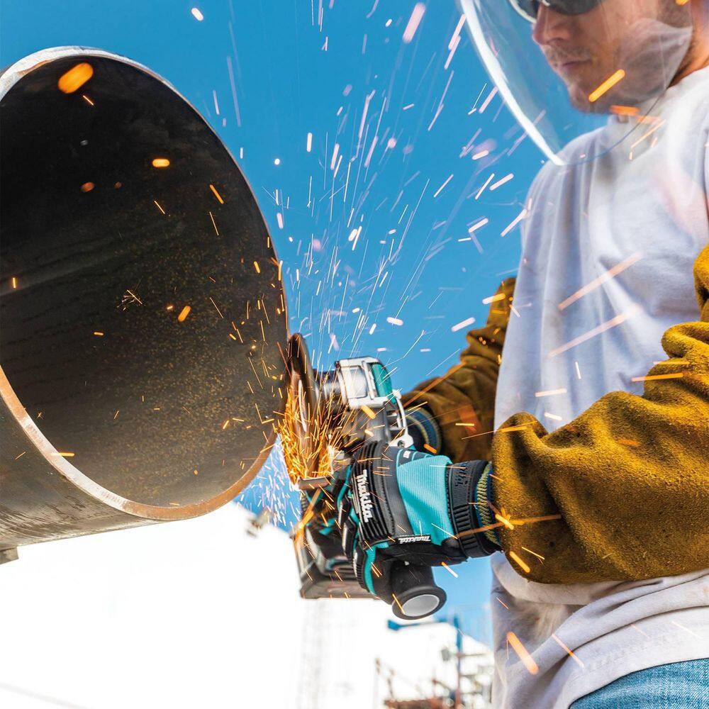 A professional technician using the Makita GAG11M1 40V Max XGT brushless 5-inch angle grinder to smooth industrial steel, demonstrating the high-performance cordless power and control provided by the ergonomic side handle.