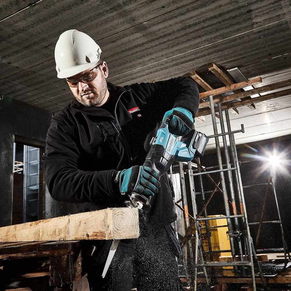 A professional wearing a hard hat and safety glasses using the Makita GRJ01 reciprocating saw to cut through heavy lumber, highlighting the tool's power and stability during demolition.