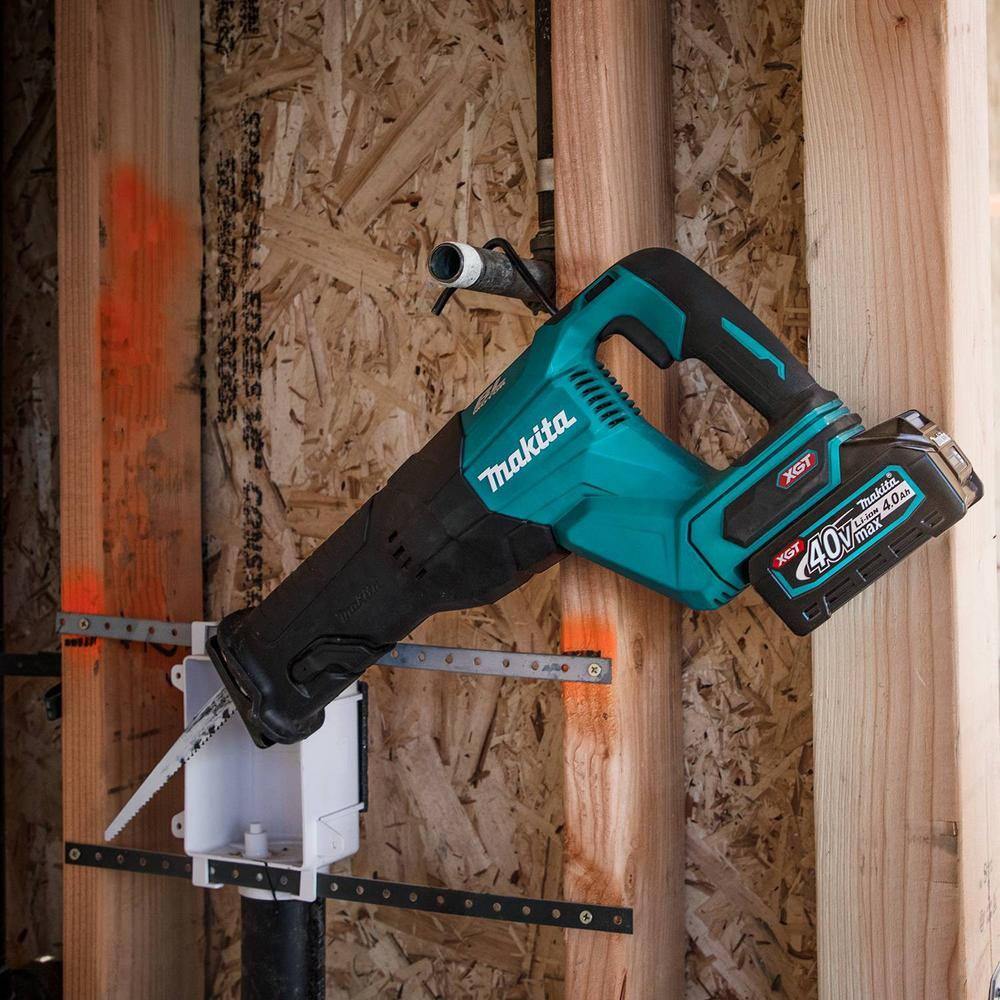 An action photograph showing the Makita GRJ01M1 reciprocating saw hanging from a metal conduit by its retractable tool hook near a wall stud, illustrating efficient tool management on the job.