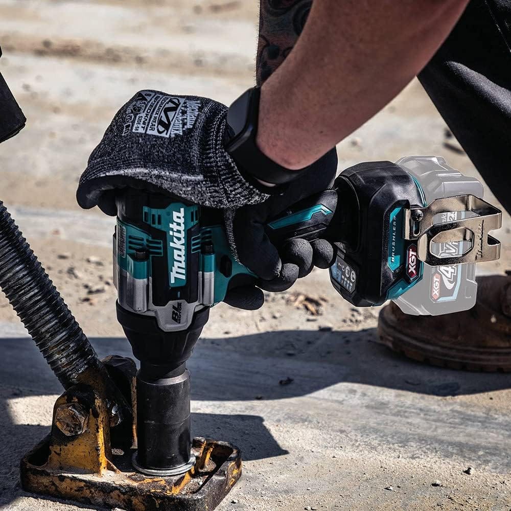 A worker wearing a knit industrial glove uses the Makita GWT08Z cordless 1/2 inch impact wrench to tighten a large heavy duty bolt on a concrete surface anchoring bracket. The high power cordless mechanic tool stands vertically during high torque construction installation.