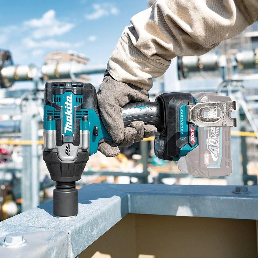 A close up action shot of a worker in protective gloves operating the Makita 40V Max XGT cordless brushless impact wrench on an outdoor structural framing project. The mid torque power tool drives an impact socket down onto a metal beam layout flange under clear daylight conditions.
