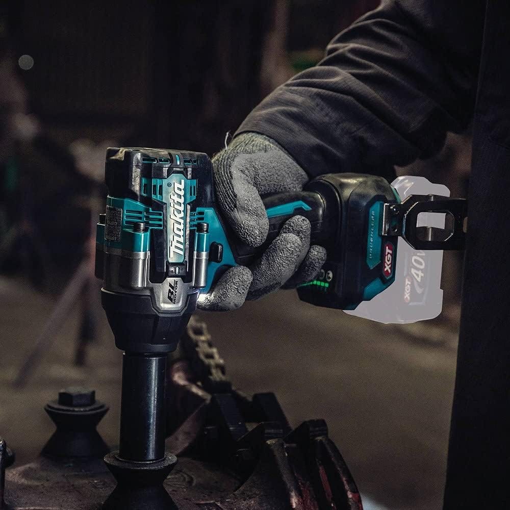 An automotive technician using the Makita GWT08Z 1/2 inch square drive cordless impact wrench inside a dimly lit workshop environment. The tool is shown under heavy operation utilizing a long deep wall socket to service commercial industrial machinery parts.