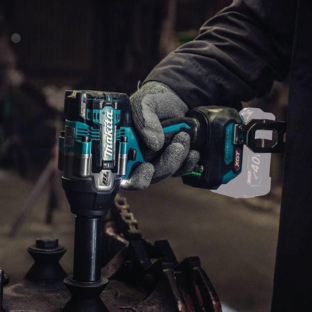 An automotive technician using the Makita GWT08Z 1/2 inch square drive cordless impact wrench inside a dimly lit workshop environment. The tool is shown under heavy operation utilizing a long deep wall socket to service commercial industrial machinery parts.