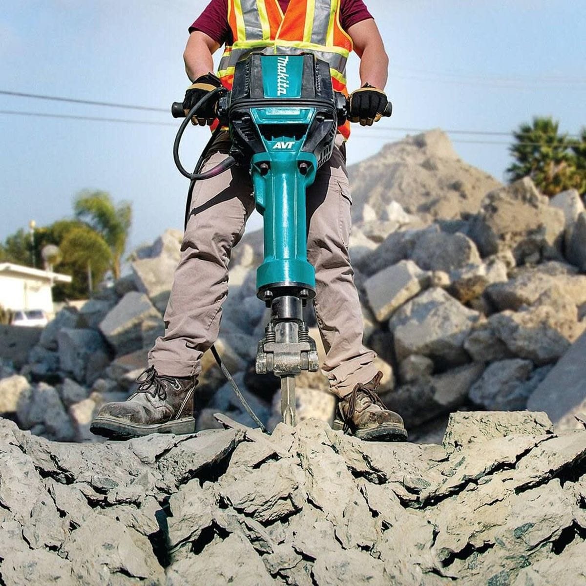 An operator using the Makita 70 lb. Advanced AVT breaker hammer to break up large piles of rocky debris on an industrial construction site, highlighting the tool's stability and power.