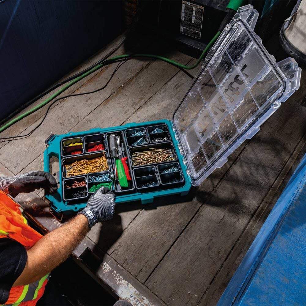 High-angle shot of a worker in safety gloves reaching into an open Makita T-90059 organizer, illustrating the accessibility of the 11 removable bins filled with sorted fasteners and electrical components.