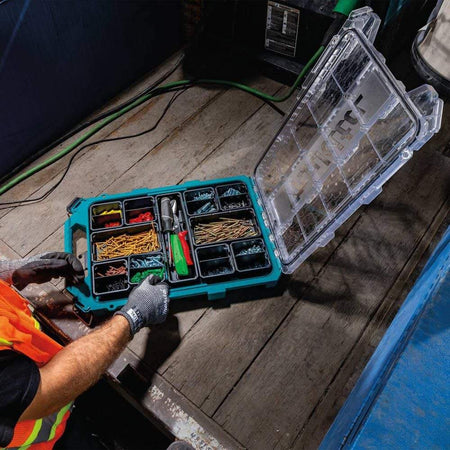 High-angle shot of a worker in safety gloves reaching into an open Makita T-90059 organizer, illustrating the accessibility of the 11 removable bins filled with sorted fasteners and electrical components.