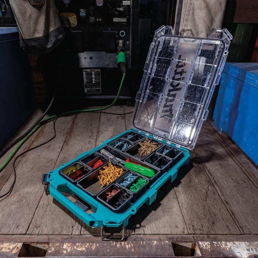 Action shot of the Makita T-90059 MAKTRAK organizer on a professional workbench, with the lid open to show bins filled with various screws, fasteners, and small tools for efficient workflow.