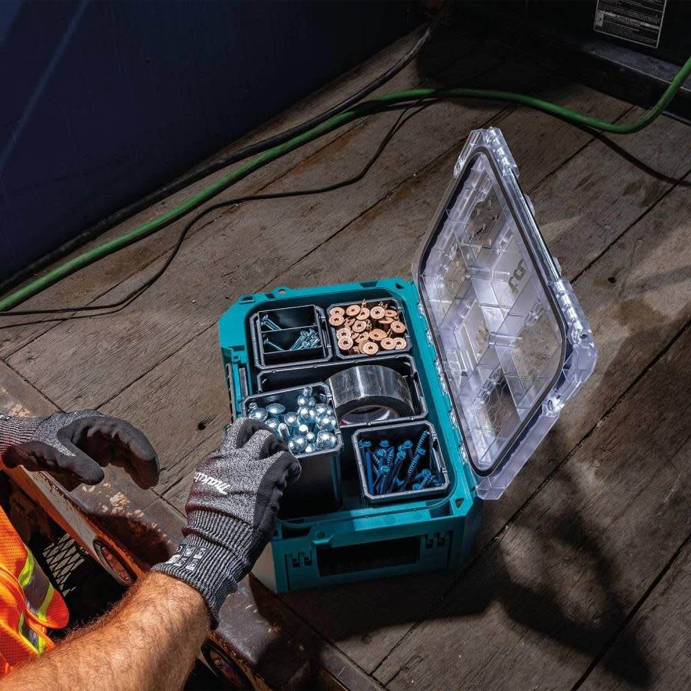 A tradesperson in safety gloves reaching into an open Makita MAKTRAK T-90065 deep compact organizer, showcasing the accessibility of the removable bins filled with fasteners, tapes, and various small parts.