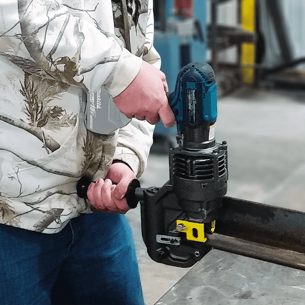 Fabricator operating the Makita XPP01ZK cordless puncher to pierce thick steel angle iron on a shop work table.