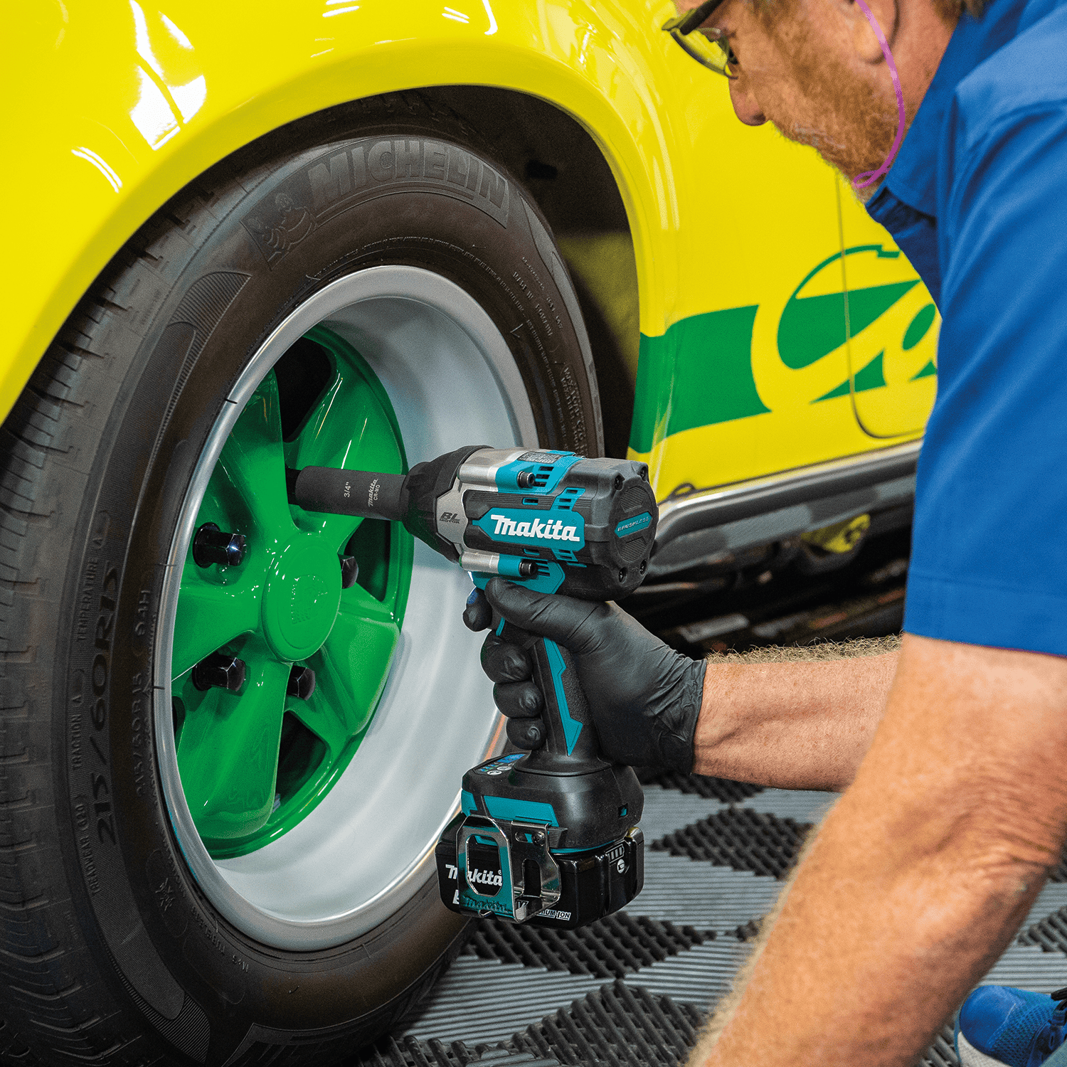 Gloved mechanic using a Makita XWT17 18V impact wrench with an impact socket to tighten wheel lug nuts on a custom sports car.
