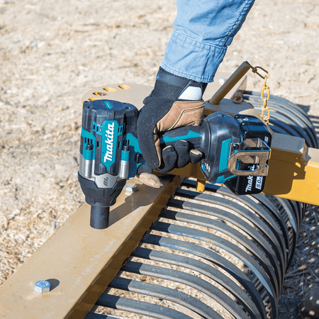 Technician driving steel frame bolts on heavy agricultural equipment using a Makita XWT17 1/2-inch mid-torque impact wrench.