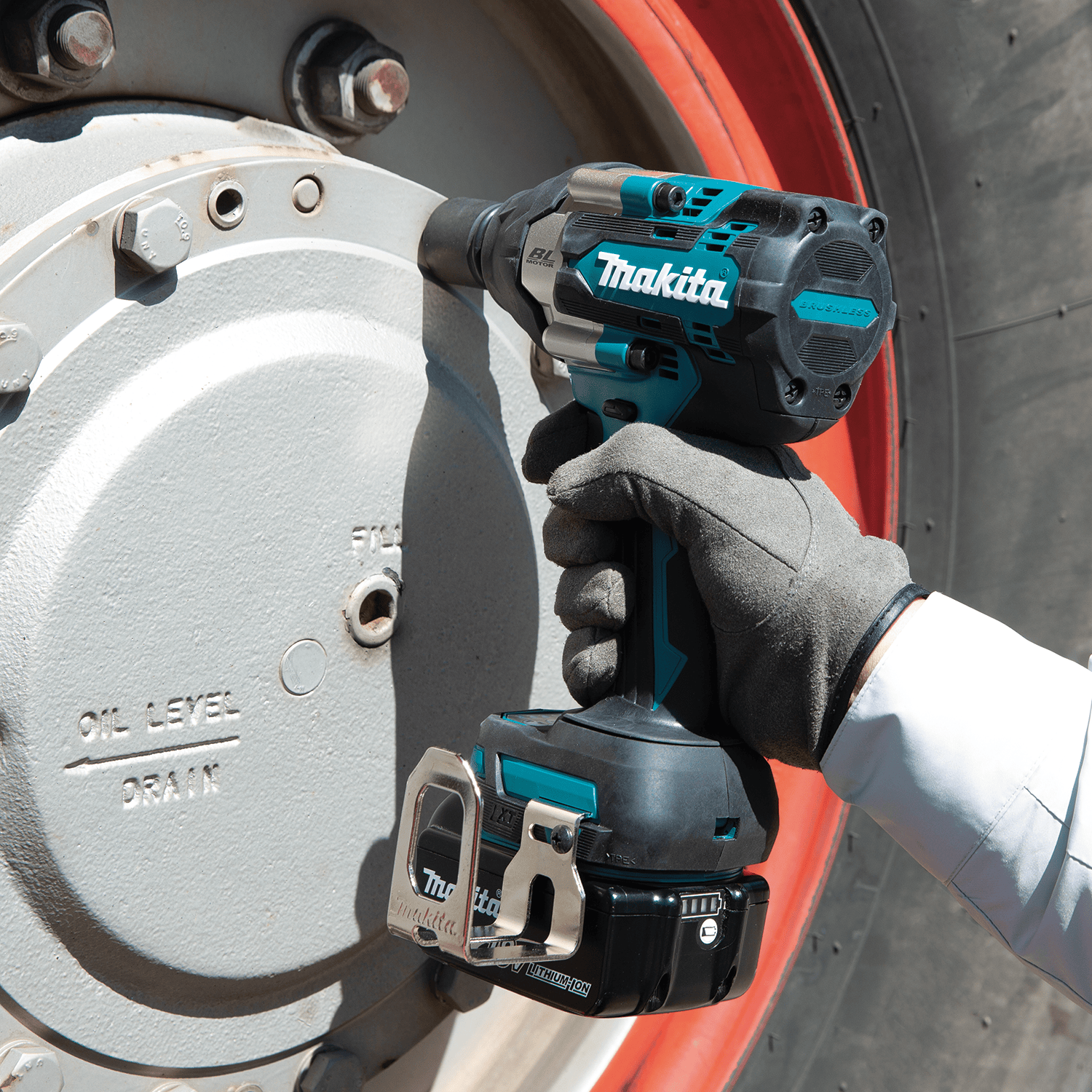 Commercial equipment technician using a Makita XWT17 cordless impact wrench to remove oil pan drain plug bolts on a heavy vehicle.