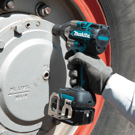 Commercial equipment technician using a Makita XWT17 cordless impact wrench to remove oil pan drain plug bolts on a heavy vehicle.