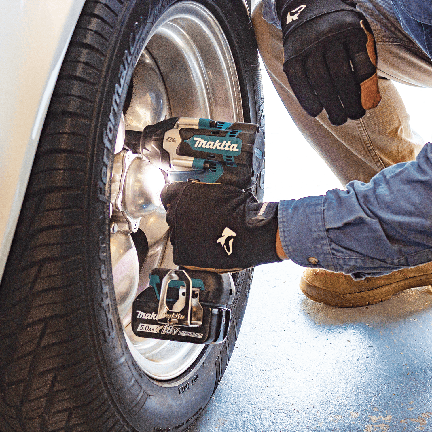 Auto mechanic loosening automotive wheel lug nuts in a shop using a Makita XWT17 18V LXT brushless mid-torque impact wrench.