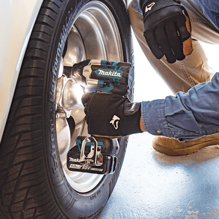 Auto mechanic loosening automotive wheel lug nuts in a shop using a Makita XWT17 18V LXT brushless mid-torque impact wrench.