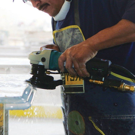 A professional stone fabricator using the Makita PW5001C wet polisher on a stone slab, demonstrating the effective water distribution and industrial power needed for a high-gloss finish.