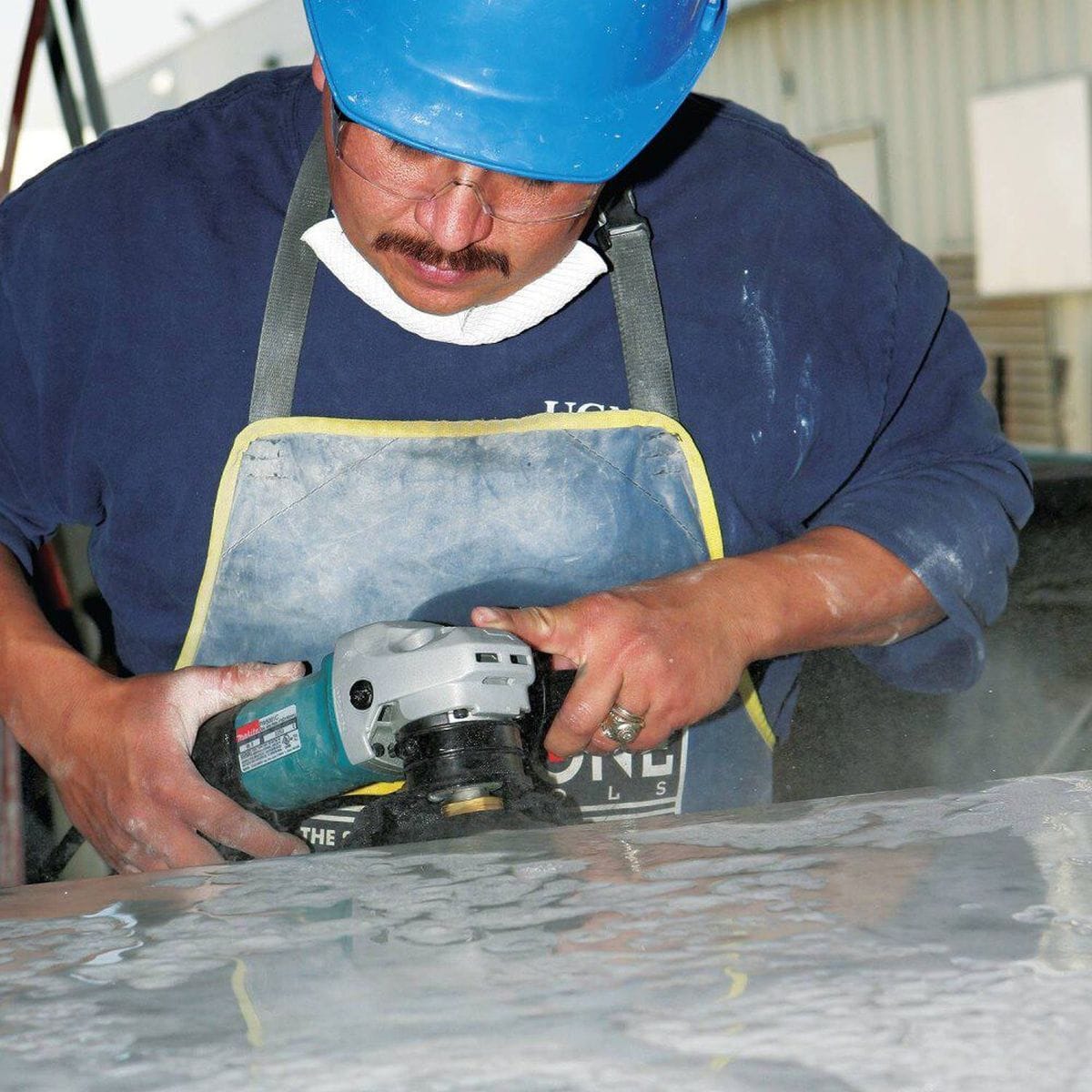 Action shot of an operator using the Makita 4-inch wet stone polisher to finish a large stone surface, highlighting the tool's maneuverability and the use of the auxiliary side handle for stability.