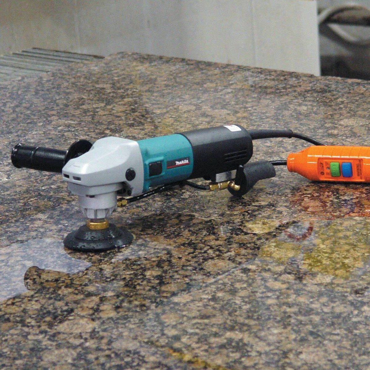 The Makita PW5001C wet stone polisher resting on a finished granite countertop, showcasing the complete professional kit including the GFCI safety plug and hook-and-loop rubber backing pad.
