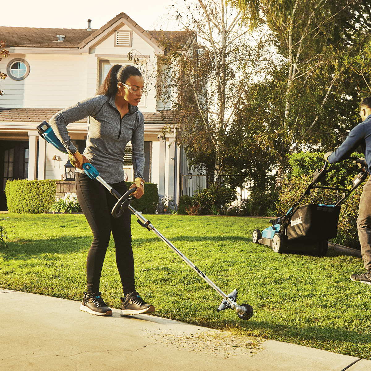 Landscaper trimming grass borders along a residential concrete driveway using the Makita 18V cordless string trimmer.