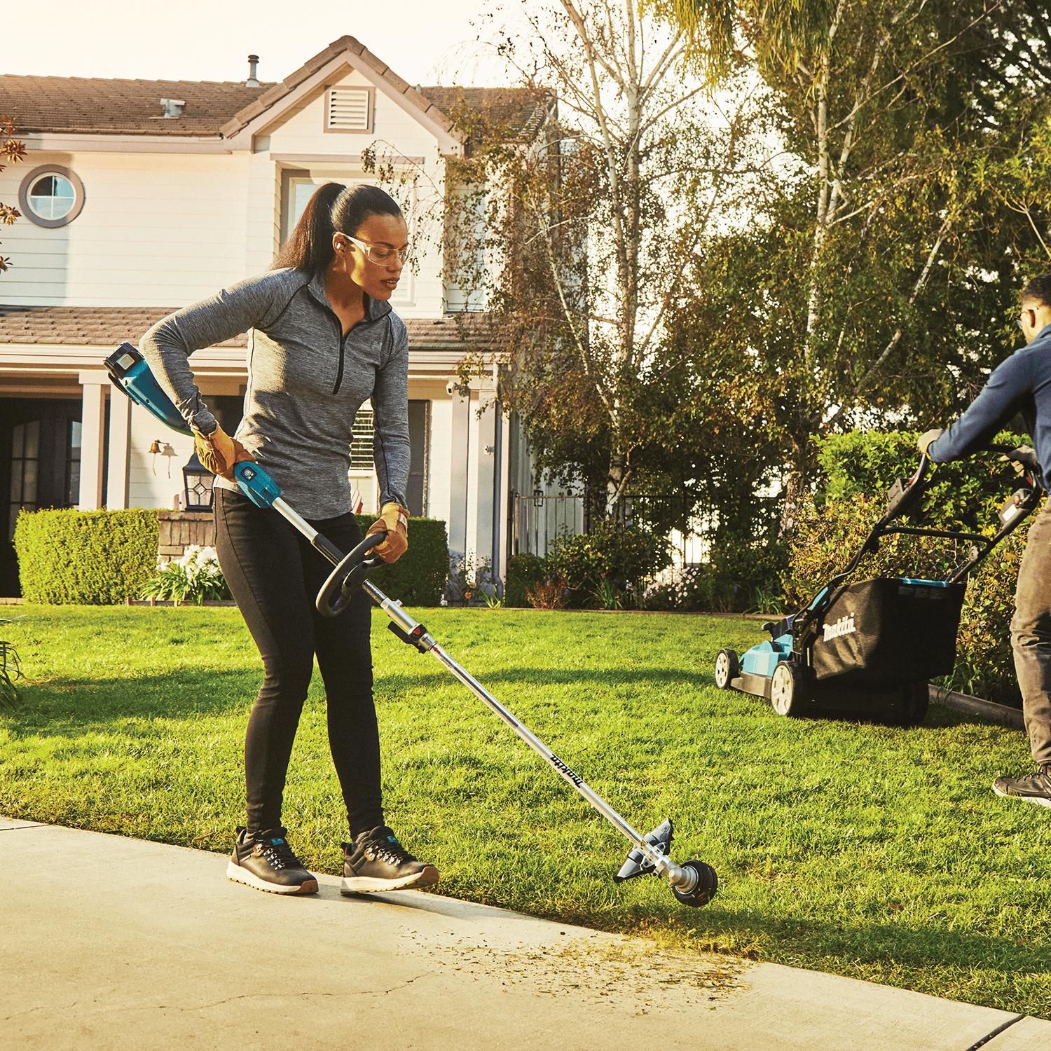 Landscaper trimming grass borders along a residential concrete driveway using the Makita 18V cordless string trimmer.