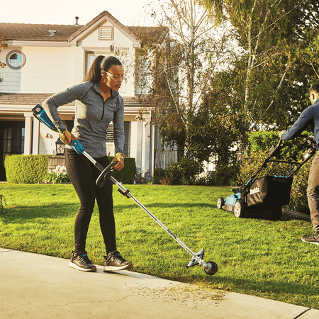 Landscaper trimming grass borders along a residential concrete driveway using the Makita 18V cordless string trimmer.