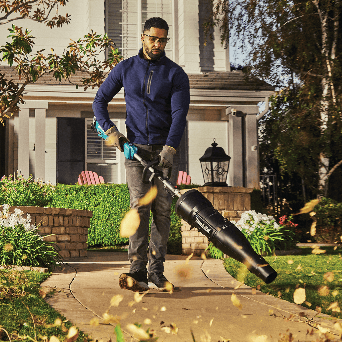 Homeowner clearing fallen autumn leaves off a paved walkway using the Makita 18V axial blower attachment.
