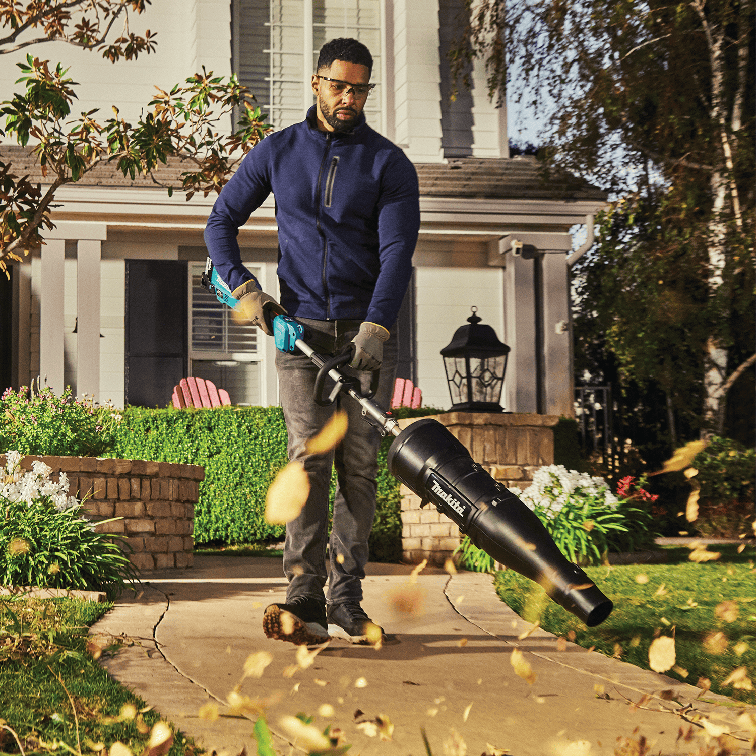 Homeowner clearing fallen autumn leaves off a paved walkway using the Makita 18V axial blower attachment.