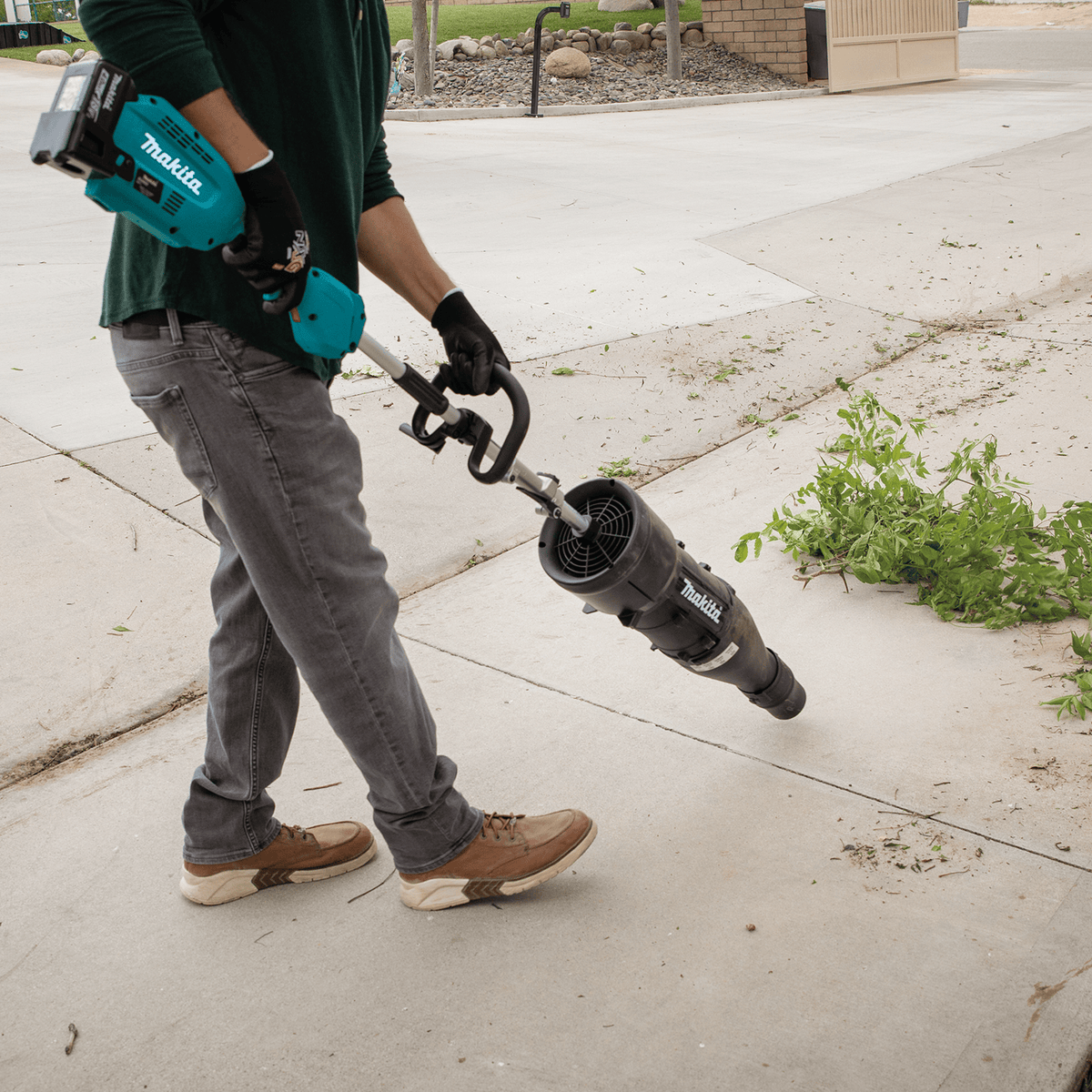Operator blowing trimmings and green debris off a concrete patio using the lightweight Makita UB401MP blower attachment.