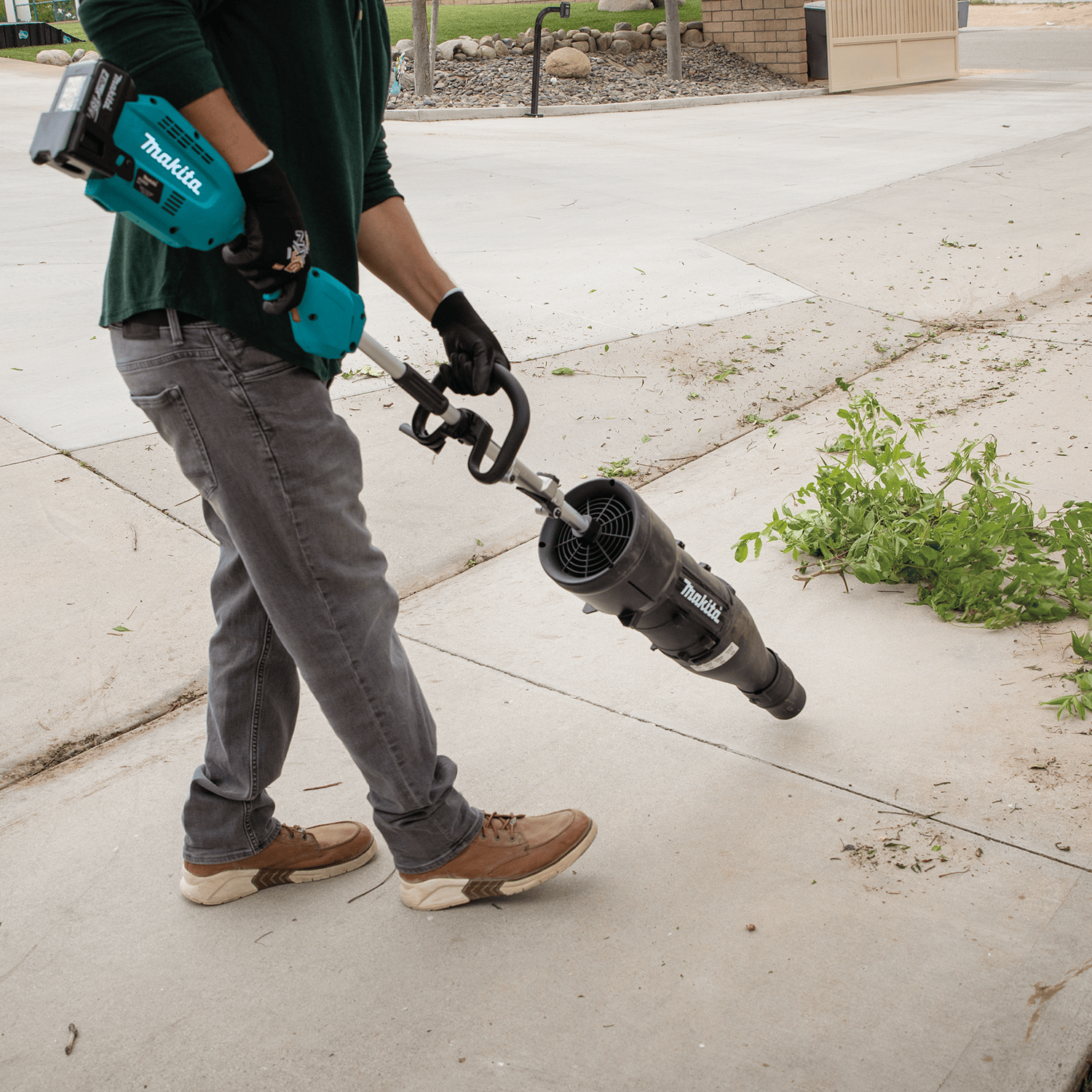 Operator blowing trimmings and green debris off a concrete patio using the lightweight Makita UB401MP blower attachment.