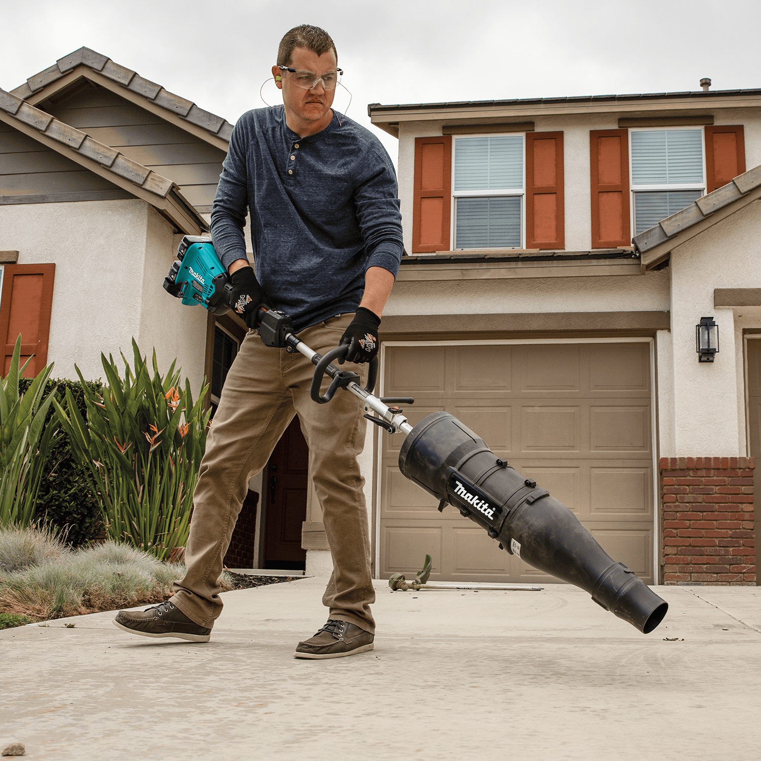 Technician sweeping driveway debris using the high-volume 438 CFM Makita 18V cordless couple shaft blower.