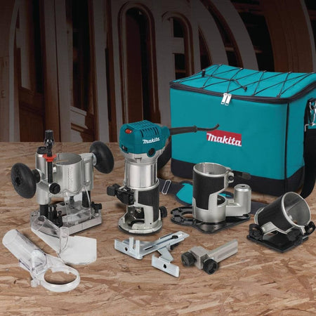 Complete Makita RT0701CX3 variable speed compact woodworking router kit laid out on a workbench, featuring the 6.5 Amp router, four specialized bases, edge guides, dust extraction attachments, and a durable teal tool bag.