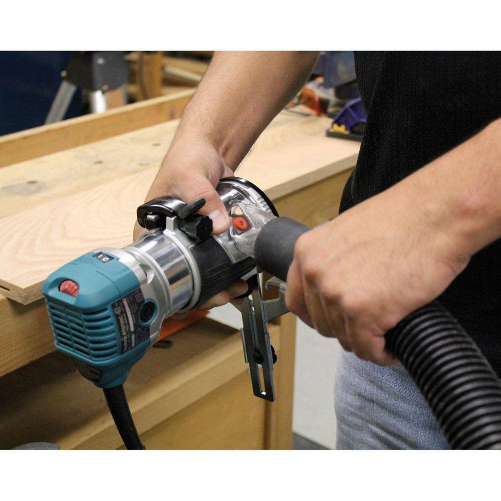 A woodworker connecting a vacuum hose to the dust extraction attachment on the Makita RT0701CX7 plunge router base for a cleaner workspace.